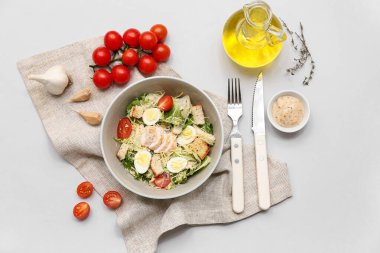 Bir kase lezzetli tavuklu Sezar salatası, domates, sarımsak ve gri arka planda bir kase sos.