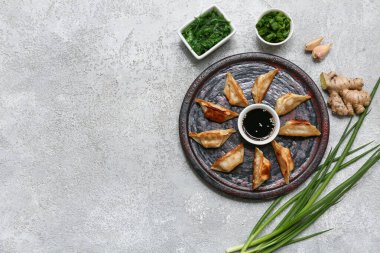 Kızarmış Japon gyoza tabağı ve bir kase yosun salatası ve gri arka planda yeşil soğan.