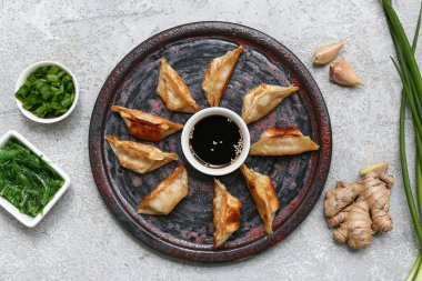 Kızarmış Japon gyoza tabağı ve bir kase yosun salatası ve gri arka planda yeşil soğan.