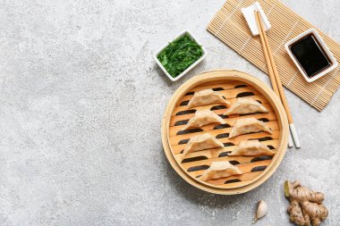 Lezzetli Japon gyozası ve bir kase soya sosu ve gri arkaplanda deniz yosunu salatası olan bambu buharı.