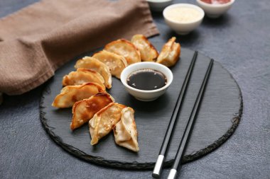 Kızarmış Japon gyozası ve koyu arkaplanda bir kase soya sosu olan kara tahta.