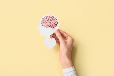 Sarı arka planda beyni olan kağıt insan kafası tutan kadın.