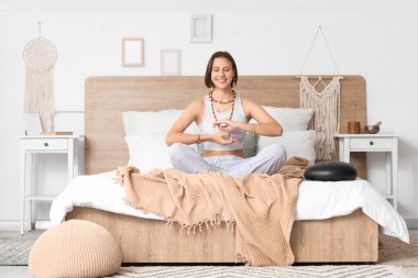 Güzel genç bir kadın evde yatakta meditasyon yapıyor.