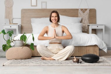 Güzel genç bir kadın yatak odasında halıda meditasyon yapıyor.