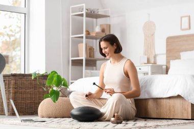 Yatak odasında halıda glukofon çalan meditasyon yapan genç bir kadın.