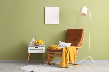 Modern odadaki yeşil duvarın yanındaki masada lamba ve taze limon tabağıyla şık bir koltuk.