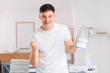 Evde demir ve giysi yığını olan yakışıklı genç adam.