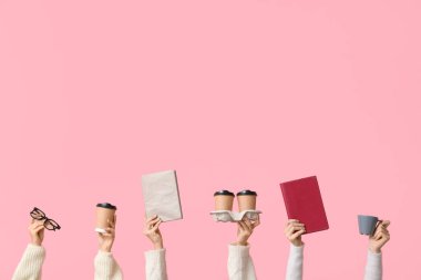 Gözlüklü kadın elleri, pembe arka planda kitap ve kahve fincanları.