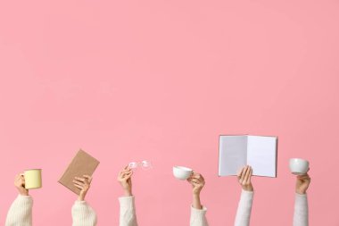 Gözlüklü kadın elleri, pembe arka planda kitap ve kahve fincanları.