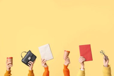 Kitaplı, çantalı, gözlüklü ve sarı arka planda kahve bardaklı kadın elleri.