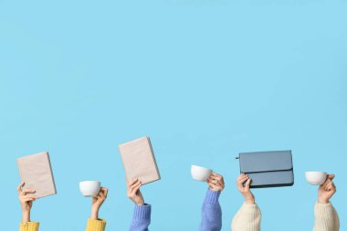 Çantalı, kitaplı ve mavi arka planda seramik kahve fincanları olan kadın eller.