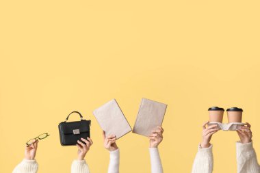 Kitaplı, çantalı, gözlüklü ve sarı arka planda kahve bardaklı kadın elleri.