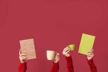 Kırmızı arka planda kitap ve kahve fincanları olan kadın eller.