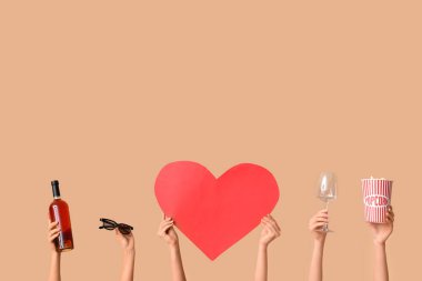 Bir kova patlamış mısır, şarap kadehi, üç boyutlu bardaklar, bir şişe şarap ve bej arka planda kağıt kalpli bir kadın eli. Sevgililer Günü kutlaması