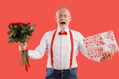 Şok olmuş olgun bir adam hediye kutusu ve kırmızı arka planda bir buket gülle. Sevgililer Günü kutlaması