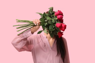 Pembe arka planda güzel kırmızı güllerle dolu buketi olan genç bir kadın. Sevgililer Günü kutlaması