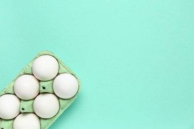 Turkuaz arka planında çiğ tavuk yumurtası olan mukavva tutucu.