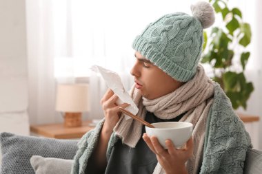 Evde hapşıran mendil ve çorbayla dolaşan hasta genç adam, yakın plan.