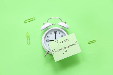 Yeşil arkaplanda TIME MANAGEMENT, alarm saati ve ataç içeren yapışkan bir not