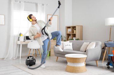Elektrikli süpürgeyle kulaklık takan yakışıklı adam evde eğleniyor.