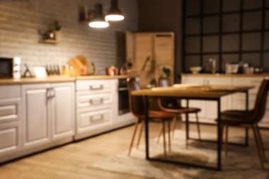 Mutfak manzarası bulanık tezgahlar, yemek masası ve akşam lambaları.