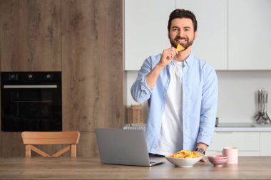 Bilgisayarlı bir adam mutfakta lezzetli cipsler yiyor.