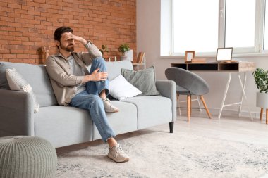 Evdeki kanepede oturan endişeli adamın portresi.