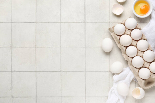 Держатель картона с сырыми куриными яйцами на белом фоне плитки