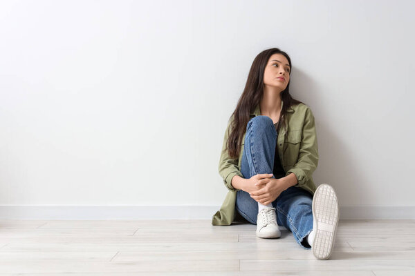 Portrait of worried young woman sitting near light wall