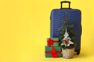 İçinde Noel ağacı olan bavul ve sarı arka planda hediyeler