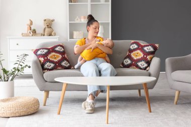 Evdeki kanepede oturan küçük, şirin bir bebeği olan mutlu bir anne.