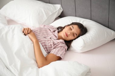 Genç ve güzel bir kadın sabahları yatakta uyuyor ve gülümsüyor.