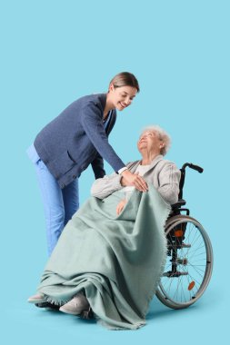 Hemşire, mavi arka planda ekoseli tekerlekli sandalyedeki yaşlı kadını koruyor.