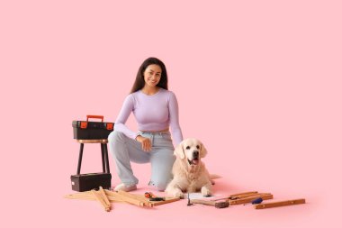 Şirin köpeği pembe arka planda mobilya montajlayan mutlu Afro-Amerikalı kadın.