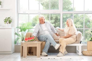 Evde kanepede oturan karpuzlu olgun bir çift.