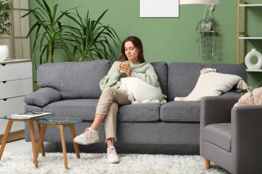 Evdeki kanepede çay içen güzel bir kadın.