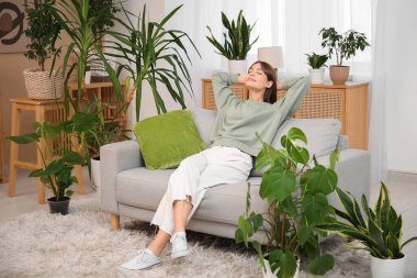 Oturma odasındaki çiçeklerin yanındaki kanepede dinlenen genç bir kadın.