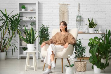 Evdeki çiçeklerin yanındaki beyaz koltukta oturan genç bayan bahçıvan.