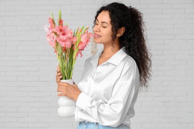 Evinde beyaz tuğla duvarın yanında pembe gladyatör çiçekleri olan güzel, mutlu bir Afro-Amerikalı kadın.