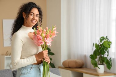 Evinde bir buket pembe gladyatör çiçeğiyle güzel, mutlu, Afro-Amerikan bir kadın.