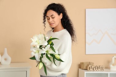 Evinde bir buket beyaz zambak çiçeğiyle güzel, mutlu, Afro-Amerikan bir kadın.