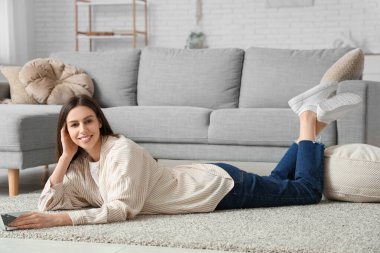 Evde yerde yatarken dizüstü bilgisayarla çalışan genç ve güzel bir kadın.