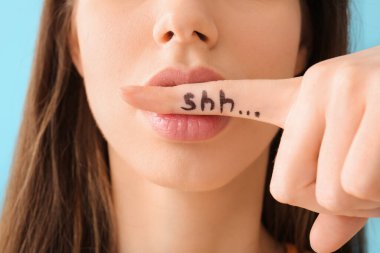 Sessiz bir kadın mavi arka planda ağzını kapatıyor, yakın plan. Dedikodu konsepti