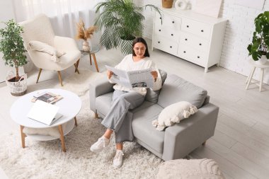 Oturma odasındaki kanepede gazete okuyan genç bir kadın.