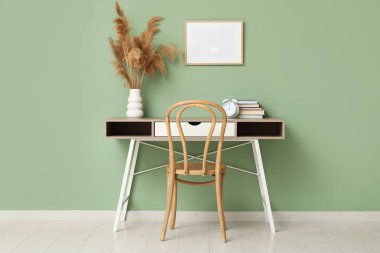 Saati, vazosu, otları ve yeşil duvarın yanındaki kitapları olan şık bir masa.