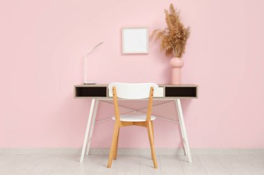 Odadaki pembe duvarın yanında vazo vazo pampa ve lamba olan şık bir masa.