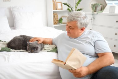 Yatak odasında kedi okuma kitabı olan son sınıf öğrencisi.