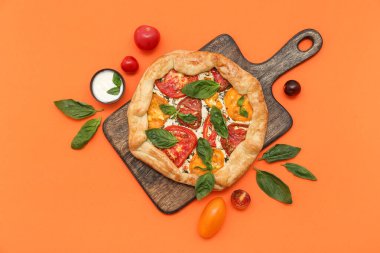 Fesleğenli ahşap domates galeti ve turuncu arka planda bir kase sos.