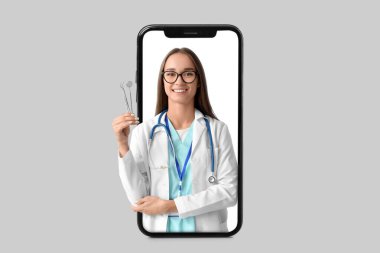 Genç bayan dişçi arka planda akıllı telefon ekranından dışarı bakıyor.