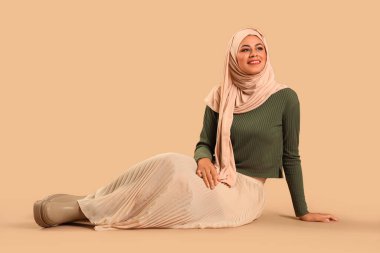 Güzel, genç, mutlu, tesettürlü Müslüman kadın kahverengi arka planda oturuyor.